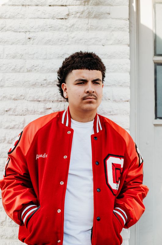 Senior in a letter jacket by a white wall